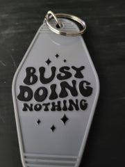 Busy Doing Nothing white motel-style keychain with bold black retro lettering and sparkle accents