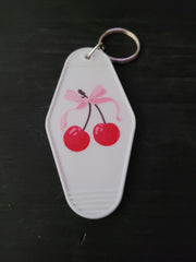 Cherry Bow white motel-style keychain with glossy red cherries tied with a soft pink bow illustration