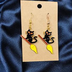 Woman wearing black cat on a broomstick enamel drop earrings