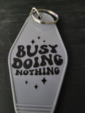 Busy Doing Nothing white motel-style keychain with bold black retro lettering and sparkle accents