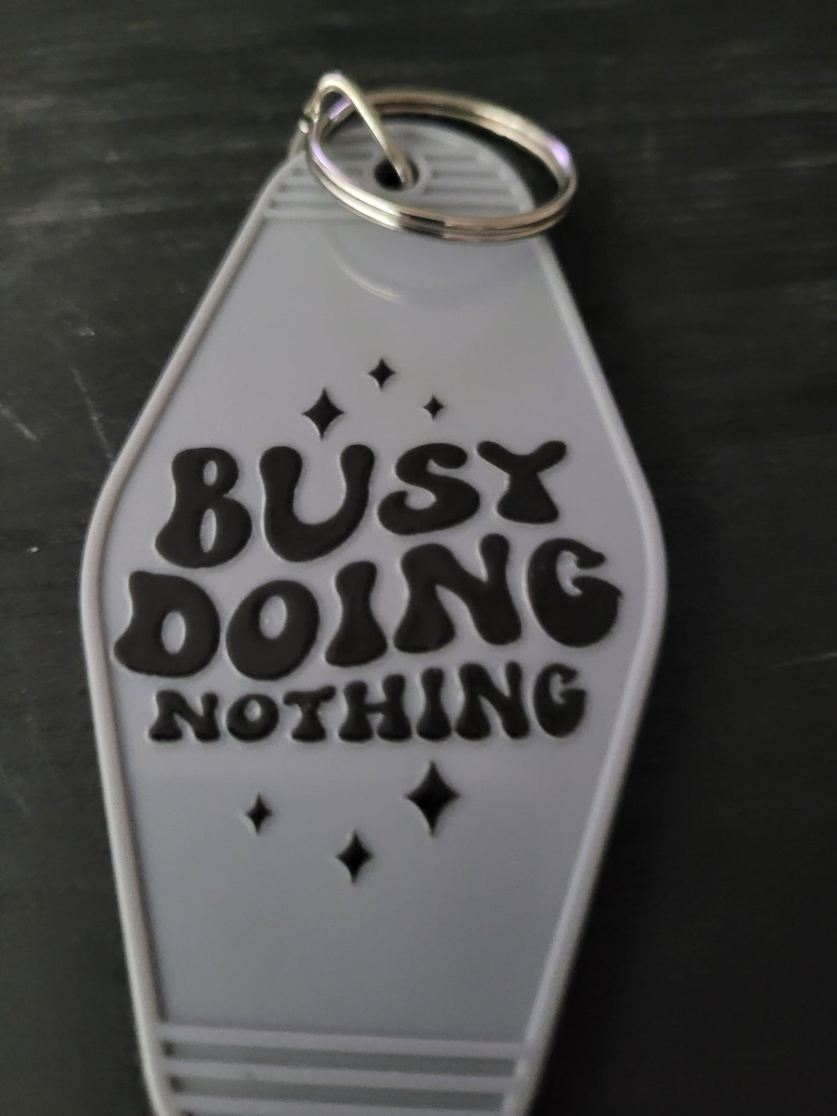 Busy Doing Nothing white motel-style keychain with bold black retro lettering and sparkle accents