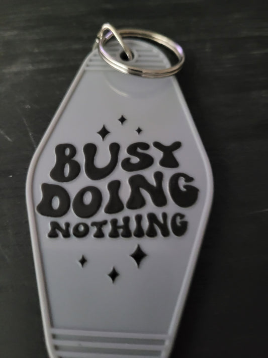 Busy Doing Nothing white motel-style keychain with bold black retro lettering and sparkle accents