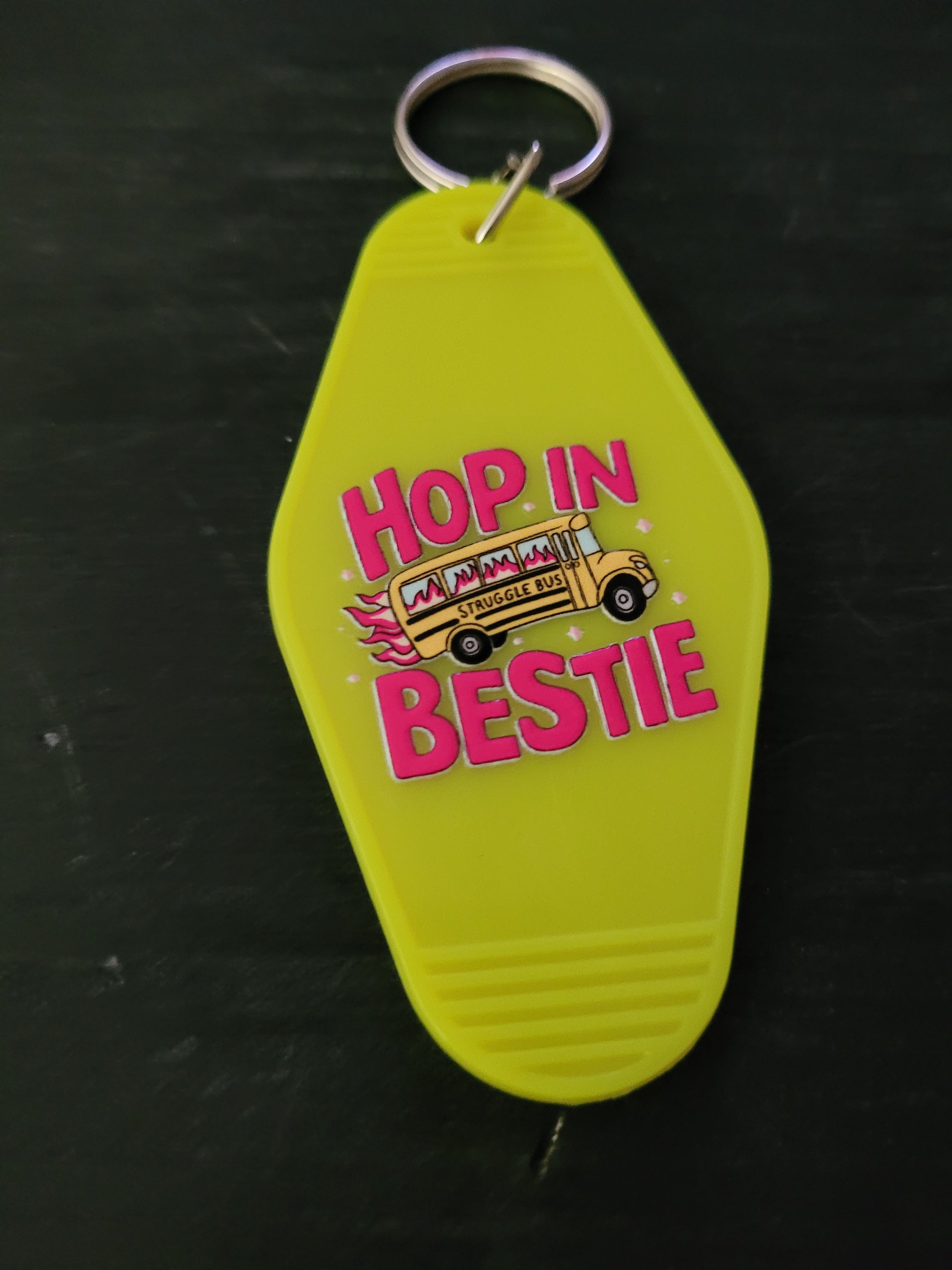Hop In Bestie neon yellow motel-style keychain with hot pink lettering and flaming Struggle Bus illustration