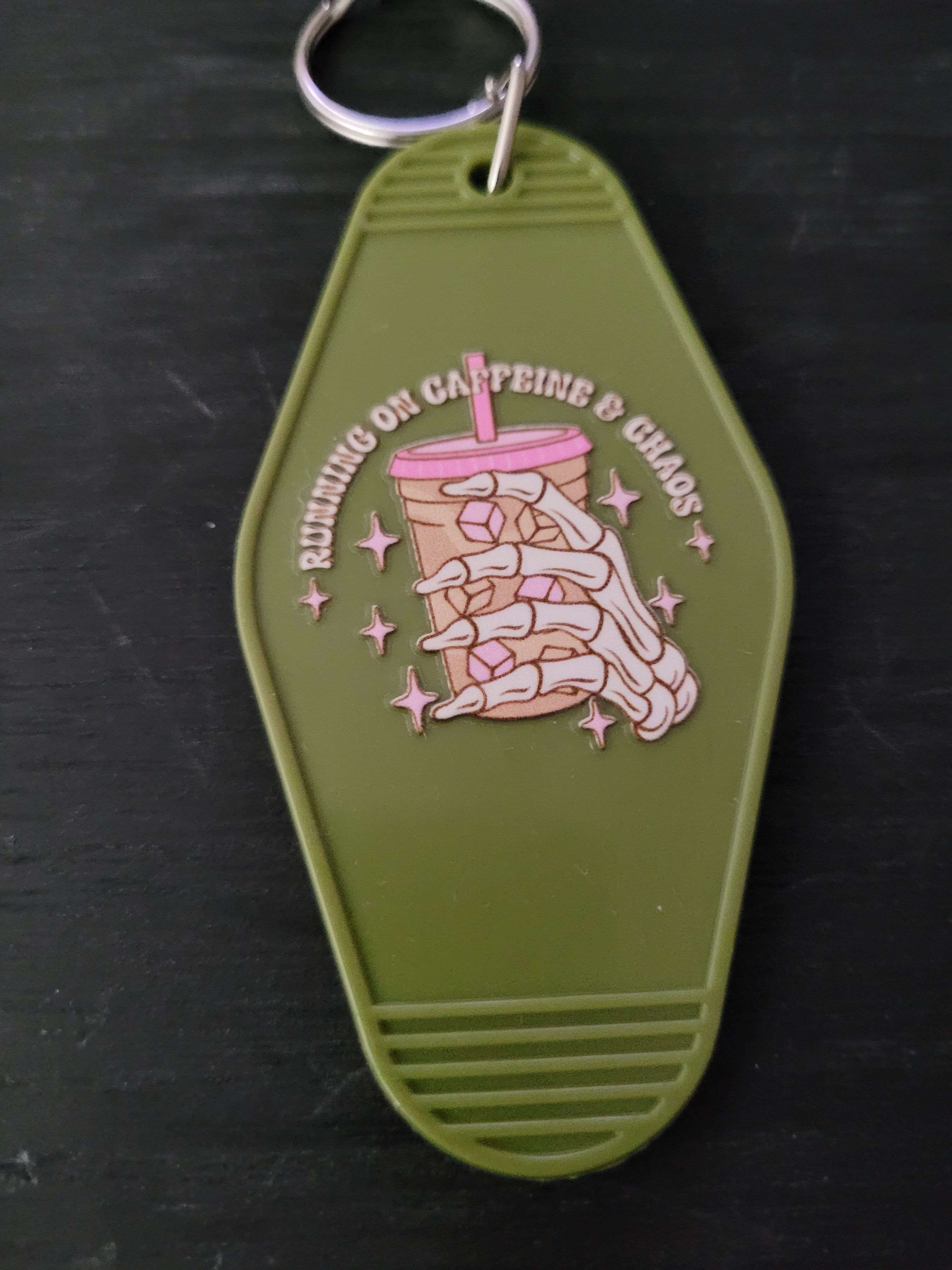 Running On Caffeine and Chaos olive green motel-style keychain with skeleton hand holding pink-lidded iced coffee and sparkle stars