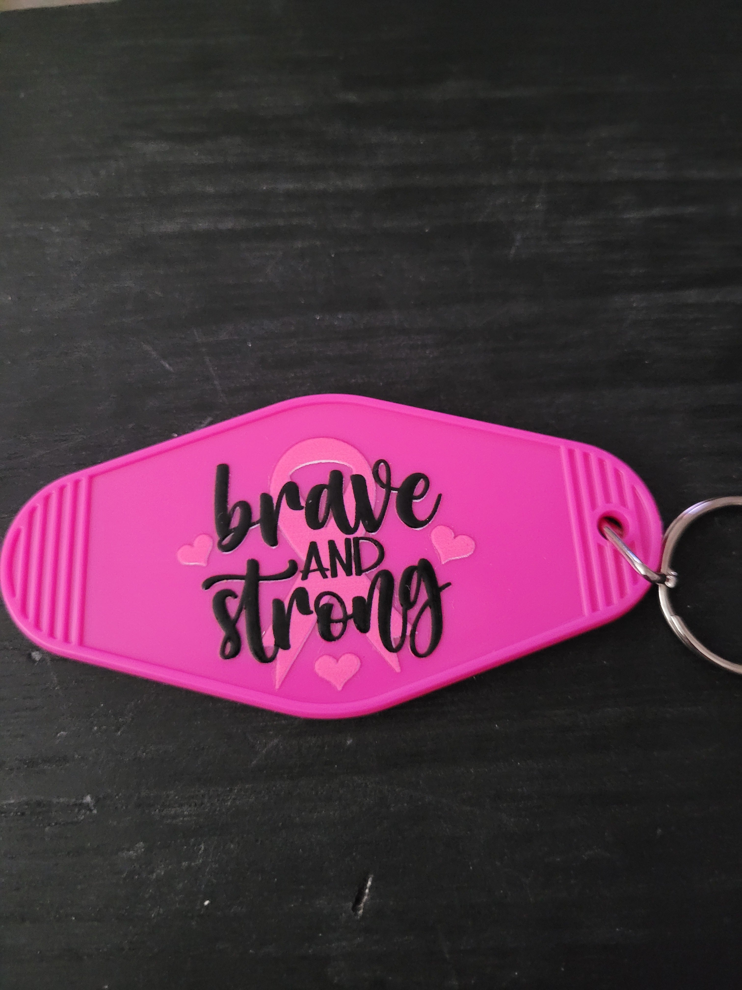 Brave And Strong hot pink oval motel-style keychain with black script lettering over pink awareness ribbon and heart accents