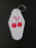 Cherry Bow white motel-style keychain with glossy red cherries tied with a soft pink bow illustration