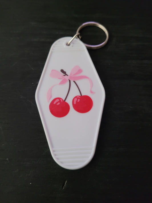 Cherry Bow white motel-style keychain with glossy red cherries tied with a soft pink bow illustration